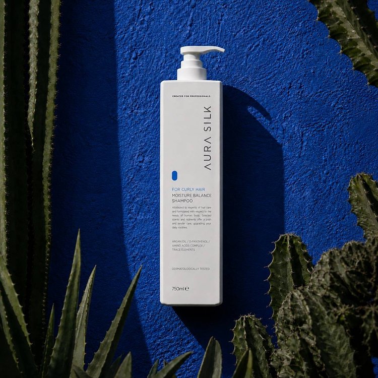 AuraSilk Moisture Balance Shampoo für lockiges Haar auf blauem Hintergrund mit Kakteen, weiße 750-ml-Flasche.
